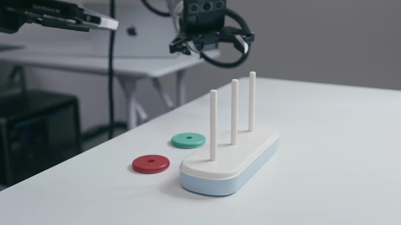 A robot gripper placing a colored ring on a wooden peg